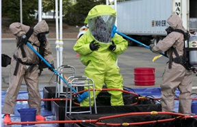 Hazardous Materials Team member in safety suit being washed for decontamination
